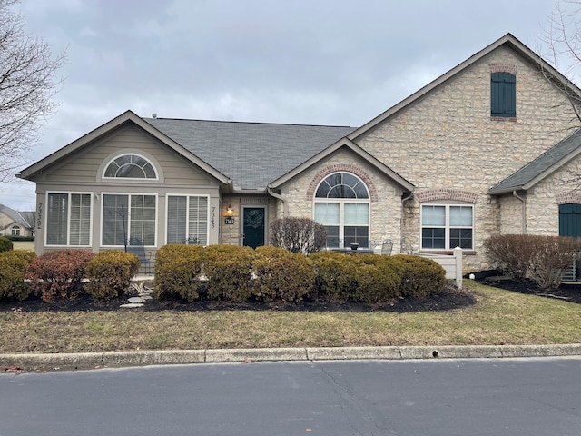 ranch-style home featuring stone siding, roof with shingles, and a front lawn