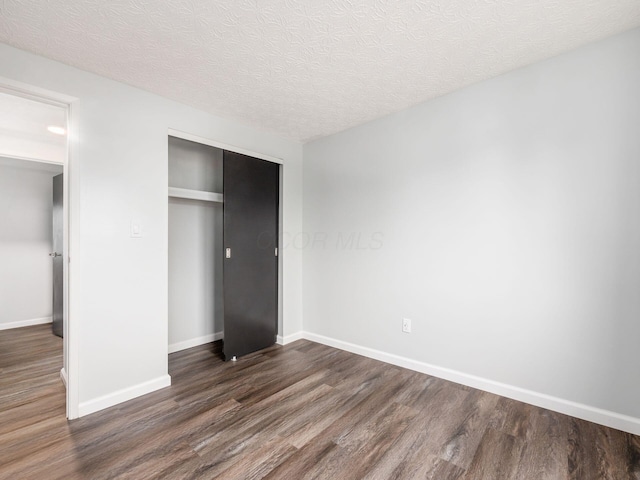 unfurnished bedroom with a textured ceiling, dark hardwood / wood-style floors, and a closet