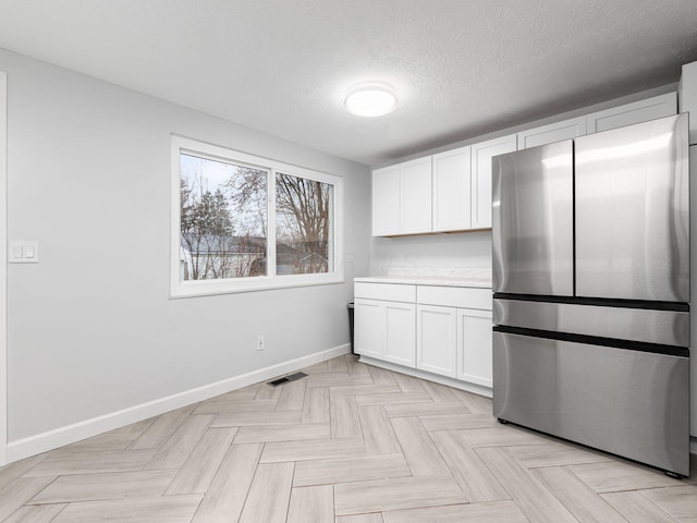 kitchen featuring a textured ceiling, white cabinetry, stainless steel refrigerator, and light parquet flooring