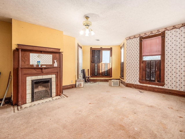 unfurnished living room with carpet flooring, a wall mounted air conditioner, a textured ceiling, a tile fireplace, and a notable chandelier