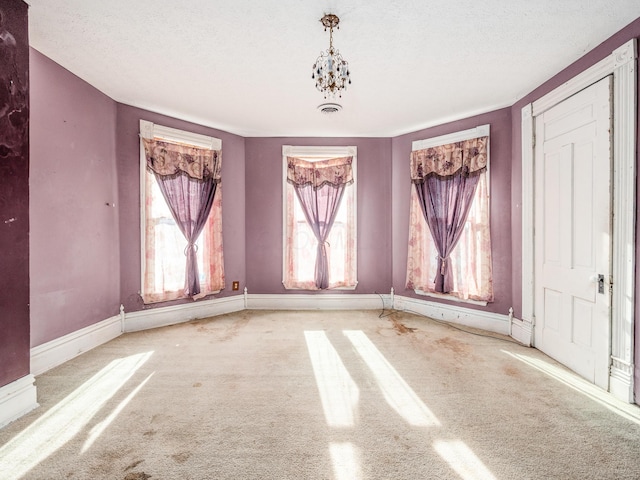 empty room featuring a textured ceiling, light carpet, and a chandelier