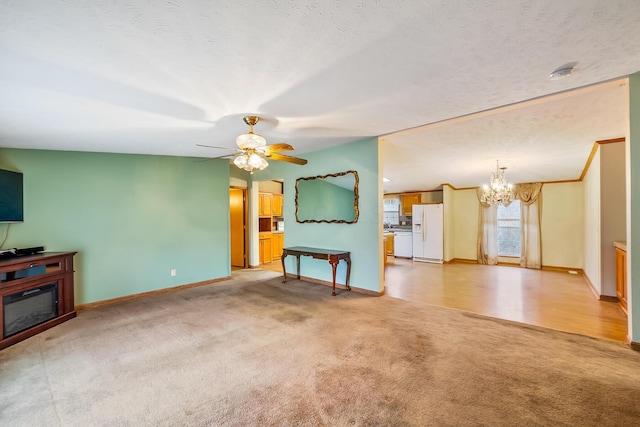 unfurnished living room with a textured ceiling, ceiling fan with notable chandelier, and light carpet