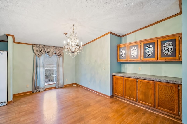 unfurnished dining area featuring crown molding, light wood-type flooring, a textured ceiling, and an inviting chandelier