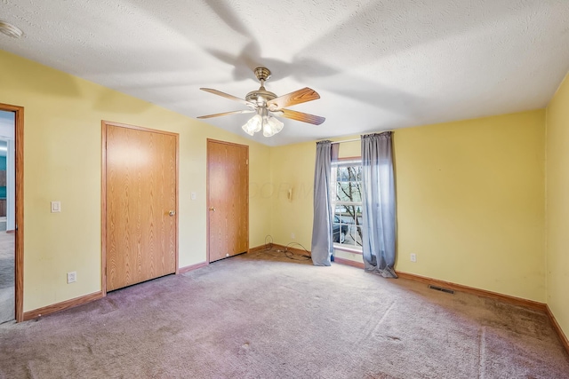 unfurnished bedroom with carpet flooring, ceiling fan, a textured ceiling, and two closets