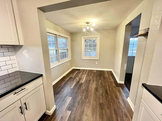 unfurnished dining area with a notable chandelier, dark hardwood / wood-style floors, and a textured ceiling