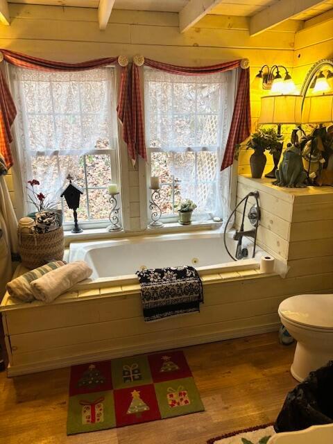 bathroom featuring beam ceiling, wood walls, hardwood / wood-style floors, and a healthy amount of sunlight