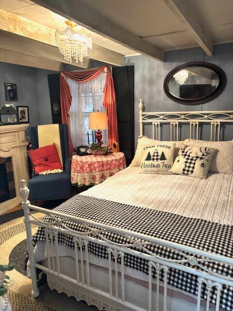 bedroom featuring beam ceiling, wooden walls, a fireplace, and an inviting chandelier