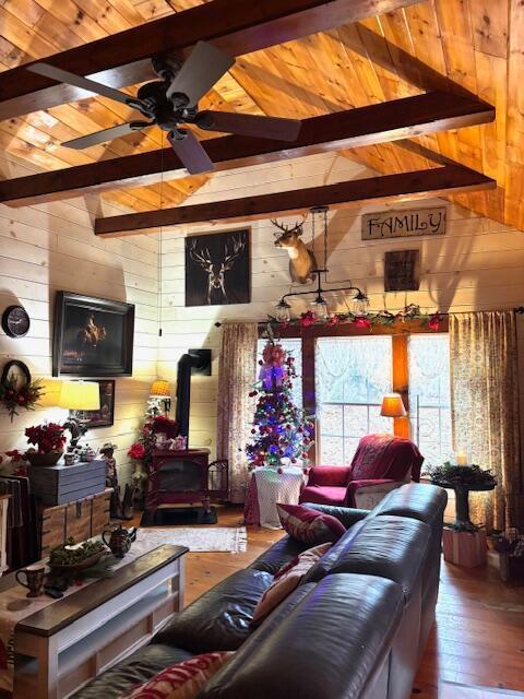 living room featuring beam ceiling, a wood stove, wood walls, and wooden ceiling