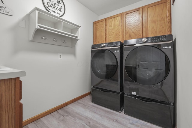 laundry area with washer and clothes dryer, cabinets, and light wood-type flooring