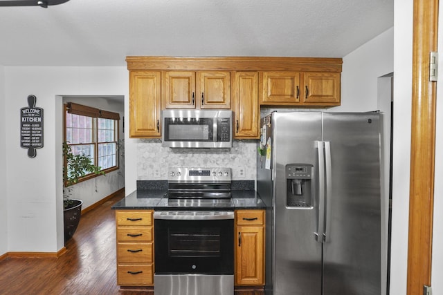 kitchen with dark hardwood / wood-style floors, decorative backsplash, appliances with stainless steel finishes, and dark stone counters