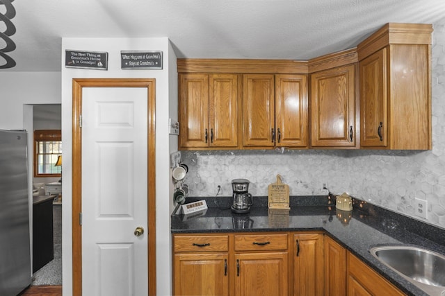 kitchen with sink, tasteful backsplash, stainless steel refrigerator, and dark stone countertops