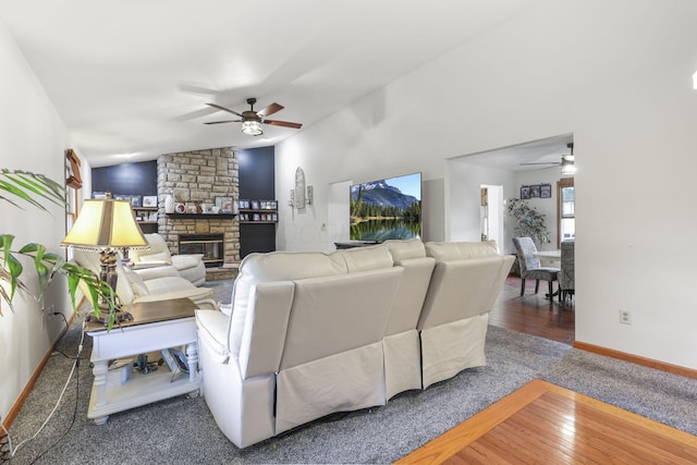 living room with ceiling fan, a stone fireplace, wood-type flooring, and vaulted ceiling