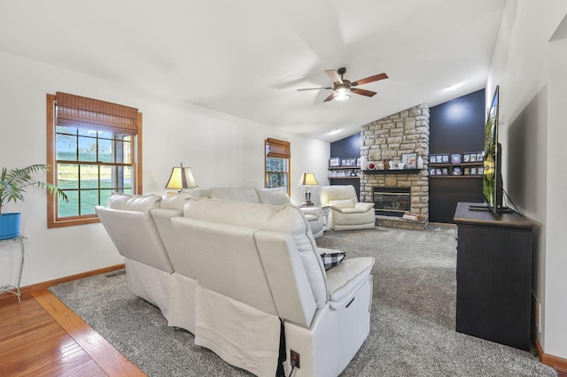 living room featuring a stone fireplace, ceiling fan, vaulted ceiling, and hardwood / wood-style flooring