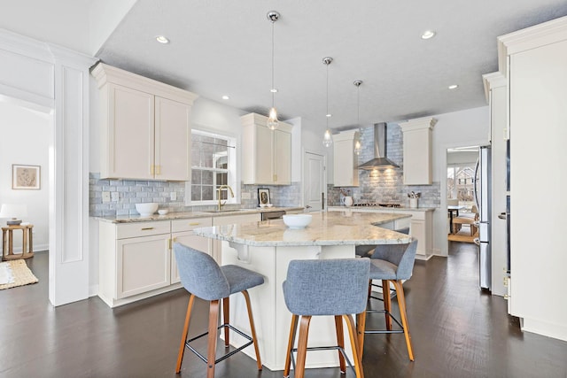 kitchen with wall chimney exhaust hood, a center island, hanging light fixtures, and white cabinets