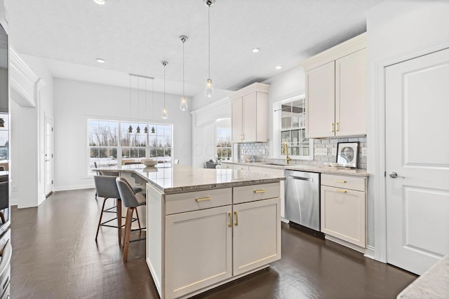 kitchen featuring decorative light fixtures, sink, a center island, stainless steel dishwasher, and light stone countertops