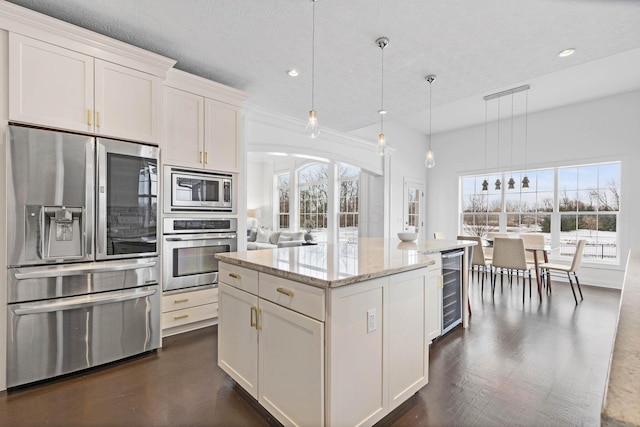 kitchen with light stone counters, decorative light fixtures, appliances with stainless steel finishes, a kitchen island, and white cabinets