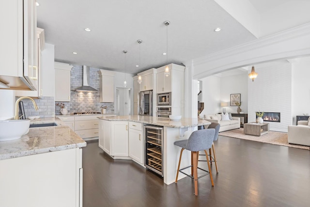 kitchen featuring pendant lighting, white cabinets, beverage cooler, a center island, and wall chimney range hood