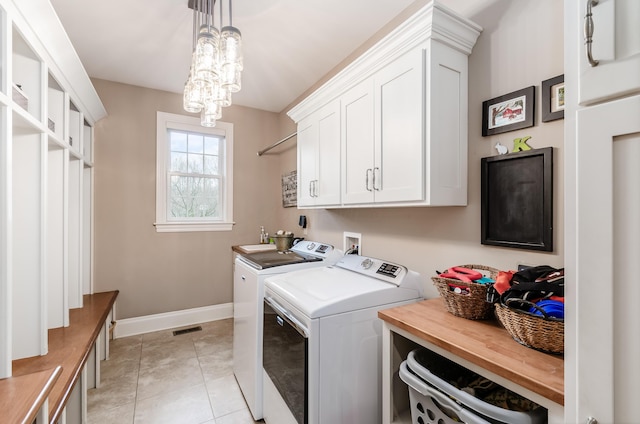 laundry area featuring cabinets, light tile patterned floors, washing machine and dryer, and a notable chandelier