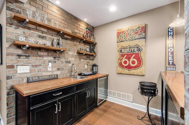 bar with wood counters, sink, light hardwood / wood-style flooring, wine cooler, and hanging light fixtures