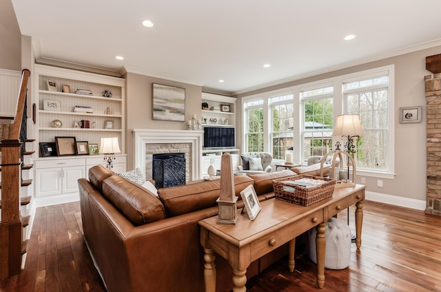 living room featuring a stone fireplace, crown molding, dark hardwood / wood-style flooring, and plenty of natural light