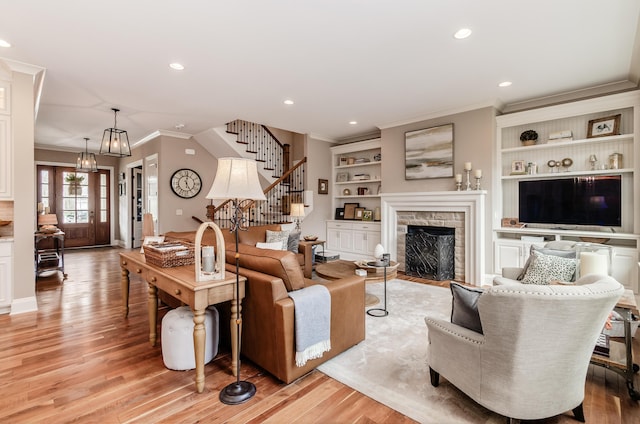 living room with a stone fireplace, crown molding, built in features, and light hardwood / wood-style flooring