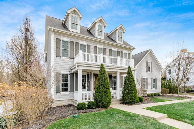 cape cod-style house featuring covered porch, a balcony, and a front yard