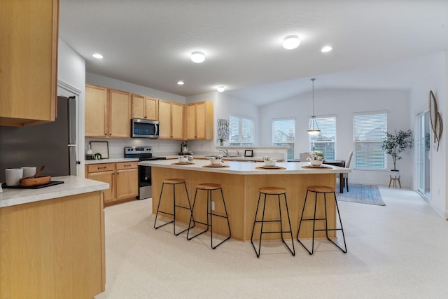 kitchen featuring light brown cabinets, lofted ceiling, hanging light fixtures, appliances with stainless steel finishes, and a breakfast bar area