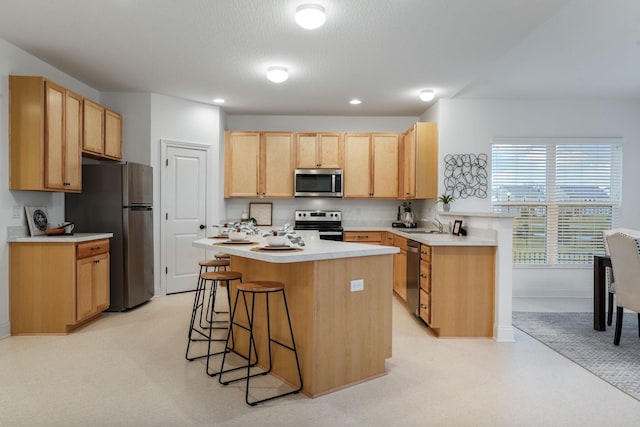 kitchen with a center island, a kitchen breakfast bar, sink, light brown cabinetry, and appliances with stainless steel finishes