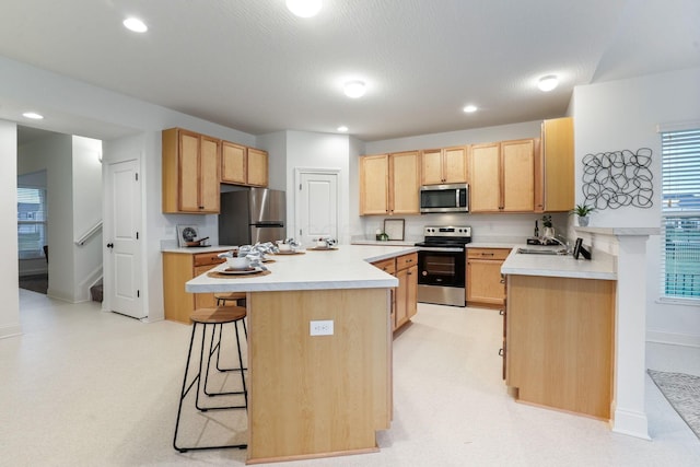 kitchen with a center island, light brown cabinets, stainless steel appliances, sink, and a breakfast bar