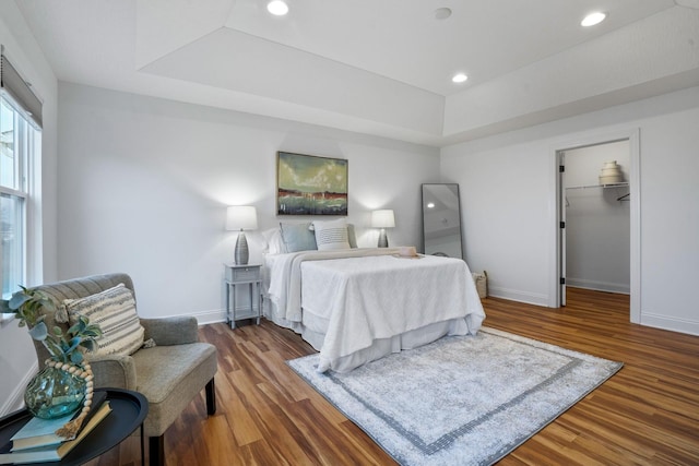 bedroom with dark hardwood / wood-style floors, a walk in closet, and a tray ceiling