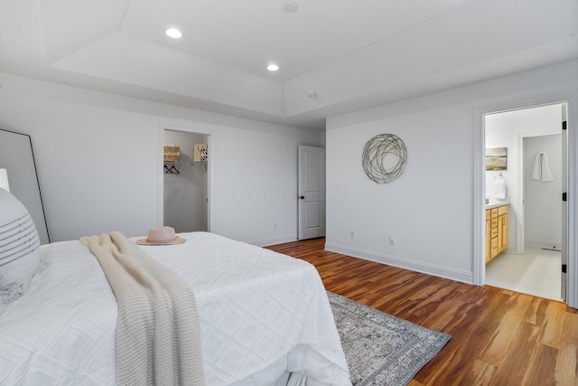 bedroom with wood-type flooring, connected bathroom, a raised ceiling, and a spacious closet