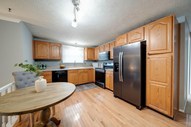 kitchen with sink, black appliances, a textured ceiling, and light hardwood / wood-style floors