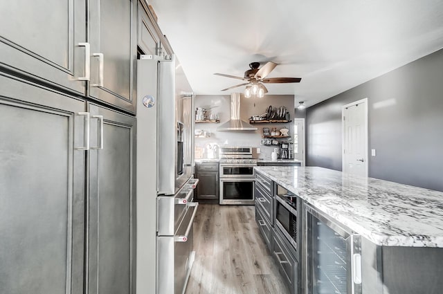 kitchen with beverage cooler, light stone counters, built in appliances, wood-type flooring, and exhaust hood