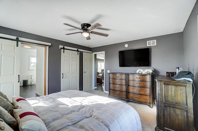 carpeted bedroom with a barn door and ceiling fan