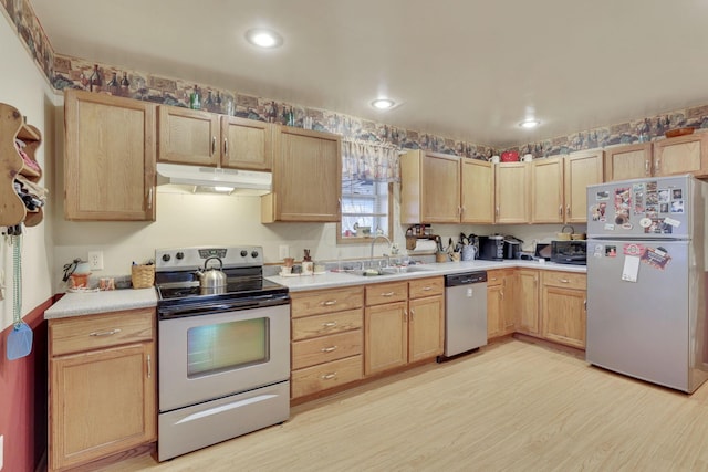 kitchen featuring light wood-style flooring, under cabinet range hood, a sink, appliances with stainless steel finishes, and light brown cabinetry