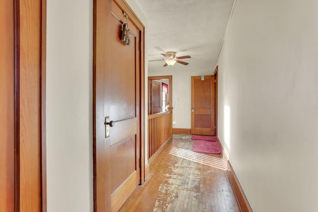 hallway with a textured ceiling, light wood-type flooring, and baseboards