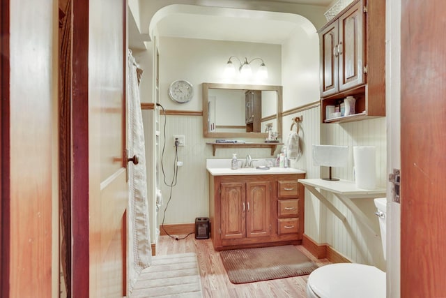 full bathroom featuring toilet, a shower with shower curtain, wood finished floors, vanity, and wainscoting