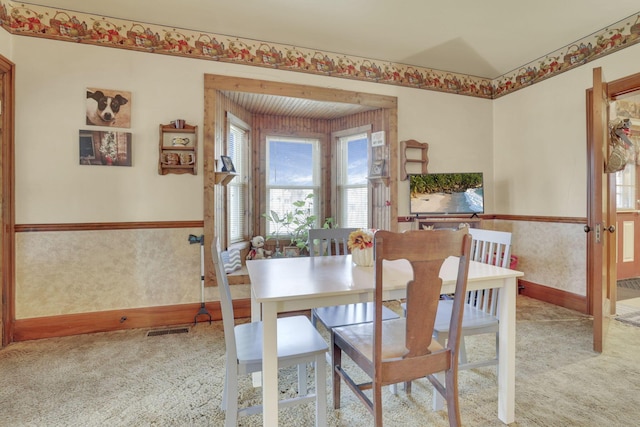 carpeted dining space featuring wainscoting, visible vents, and wallpapered walls