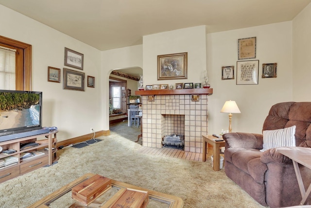 living room with carpet floors, baseboards, arched walkways, and a tiled fireplace