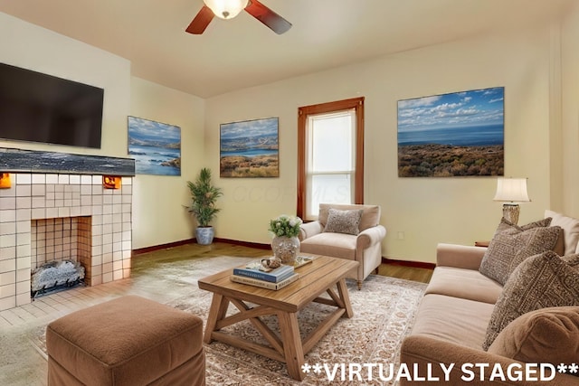 living room with ceiling fan, wood finished floors, a tile fireplace, and baseboards