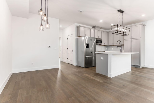 kitchen with decorative backsplash, appliances with stainless steel finishes, pendant lighting, a center island with sink, and hardwood / wood-style flooring