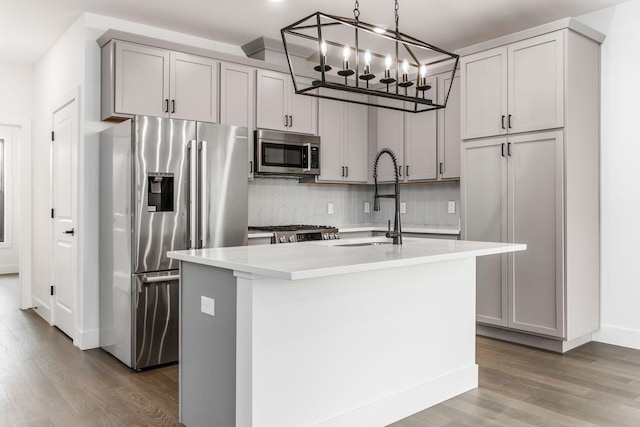 kitchen featuring gray cabinetry, a kitchen island with sink, decorative light fixtures, and appliances with stainless steel finishes