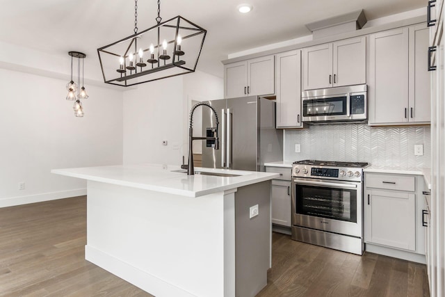 kitchen featuring pendant lighting, premium appliances, a center island with sink, and gray cabinetry