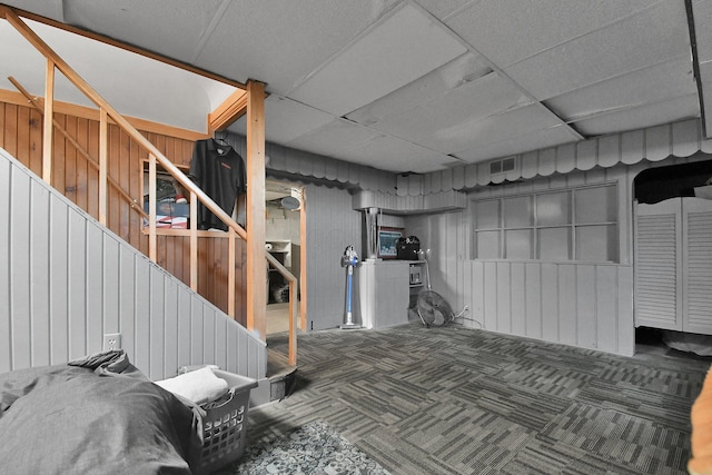 basement with dark carpet, a drop ceiling, and wood walls