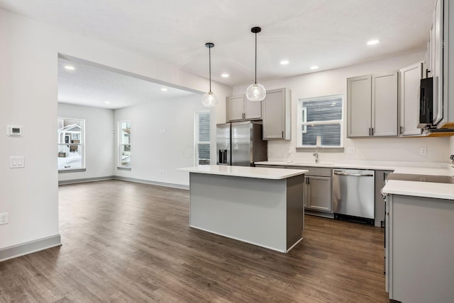 kitchen featuring dark hardwood / wood-style flooring, stainless steel appliances, gray cabinets, a kitchen island, and hanging light fixtures