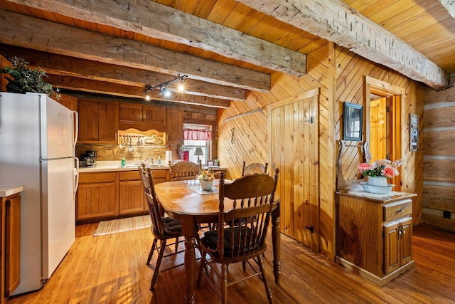 dining room featuring wooden walls, beam ceiling, and light wood-type flooring