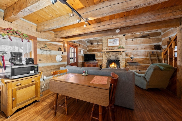 dining area featuring hardwood / wood-style floors, track lighting, log walls, beamed ceiling, and a fireplace