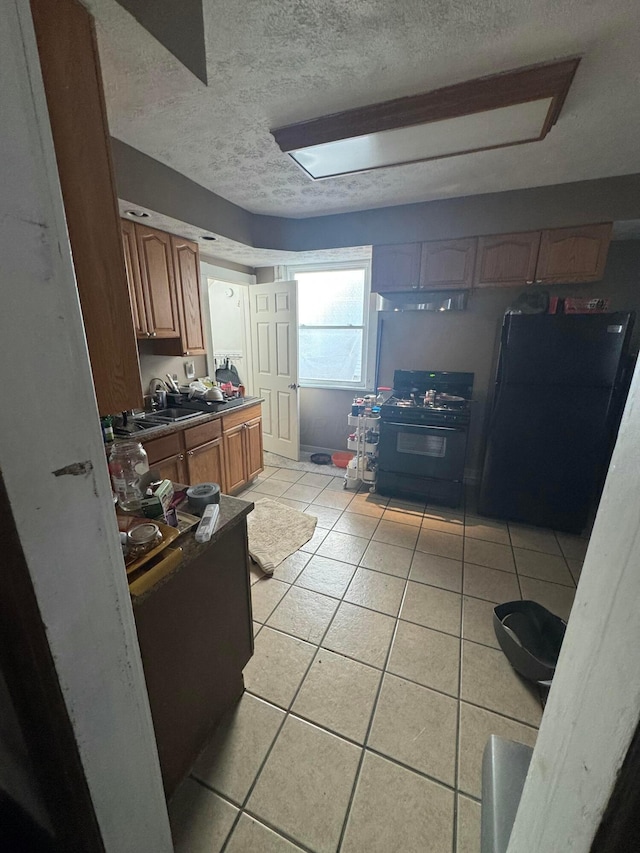 kitchen with black appliances, light tile patterned flooring, sink, and a textured ceiling