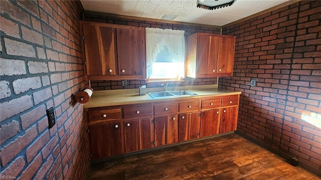 kitchen featuring a textured ceiling, sink, brick wall, and dark wood-type flooring