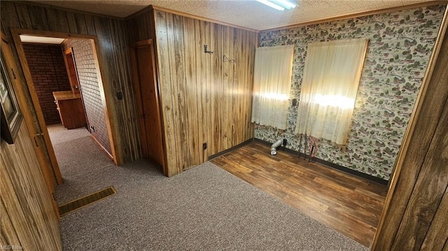 unfurnished room featuring hardwood / wood-style floors, wood walls, ornamental molding, and a textured ceiling